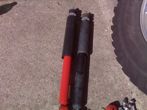2008 Jeep Wrangler - Two shock absorbers, one red and one black, are laid out on a concrete surface next to a tire. The shocks appear to be aftermarket parts.