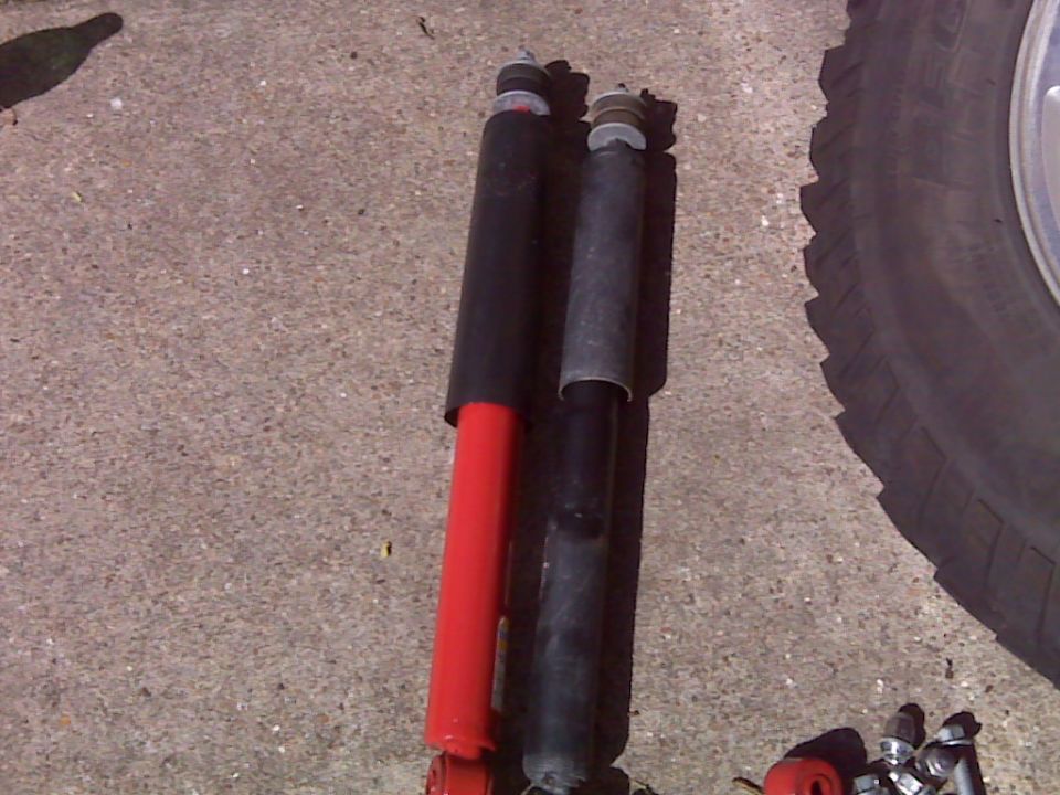 Two shock absorbers, red and black, next to a tire.