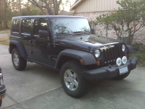 2008 Jeep Wrangler - A black 2008 Jeep Wrangler is parked on a concrete driveway in front of a brick house. The Jeep is a four-door model with tinted windows an…