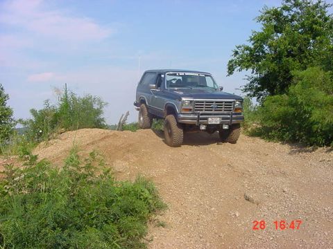 1986 Ford Bronco - A blue Ford Bronco is shown off-road on a sunny day.