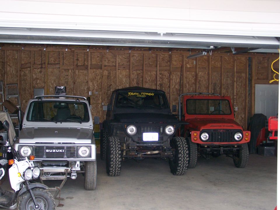Three Suzuki Samurai vehicles parked in a garage, front view.