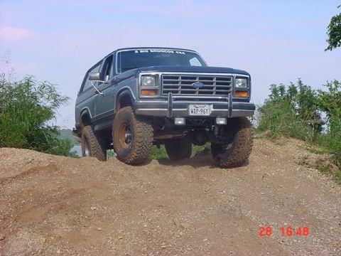 1986 Ford Bronco - A Ford Bronco navigates an off-road trail under a clear sky.