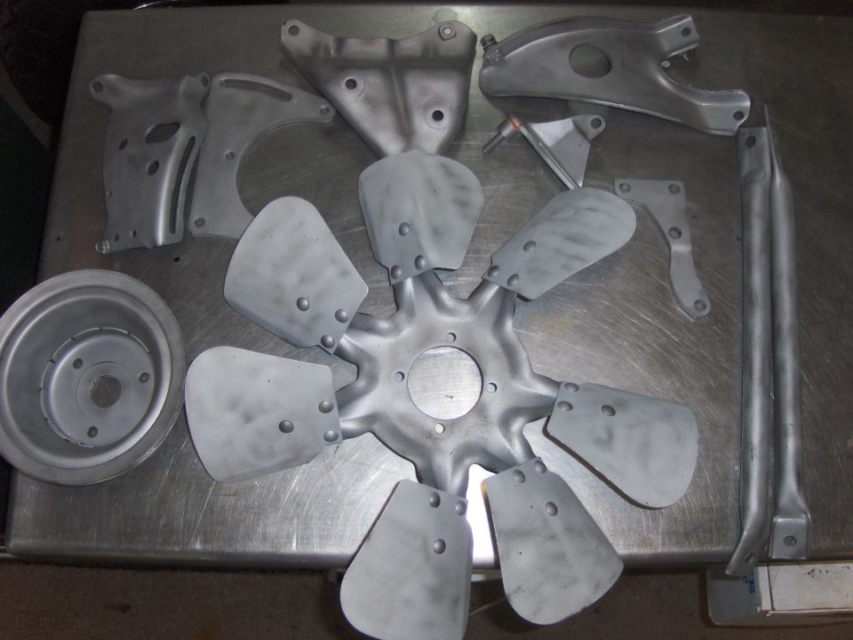 Various automotive parts including a fan, pulley, and brackets on a metal surface.