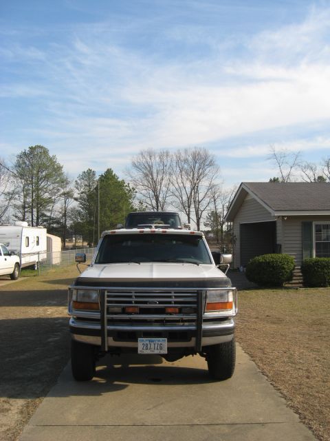1978 Ford Bronco - A white Ford F-Series truck is parked on a concrete driveway in front of a house and a camper.