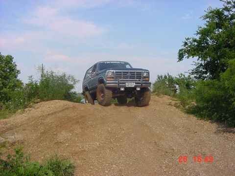 1986 Ford Bronco - A lifted 1986 Ford Bronco navigates an off-road dirt hill under a blue sky.
