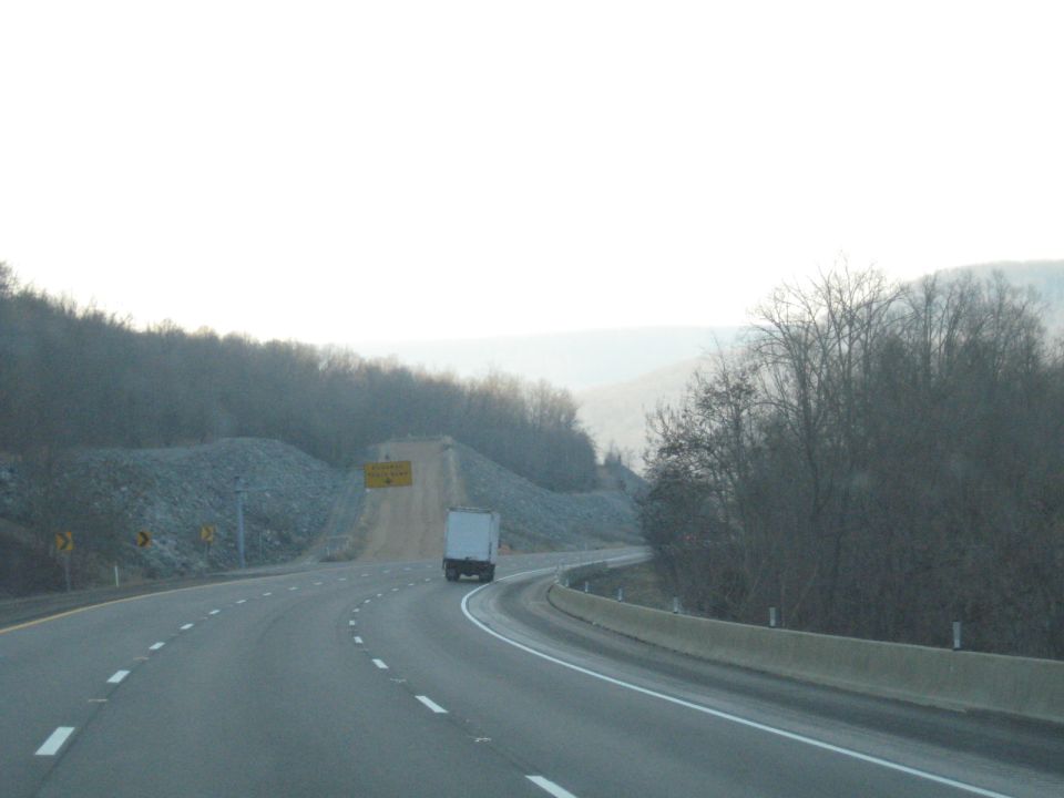 Box truck on a highway with a curve warning sign and hills