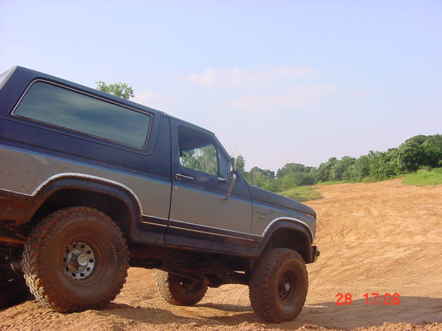 Lifted two-tone Ford Bronco angled on a sandy dirt bank, close side view of hardtop and mud tires