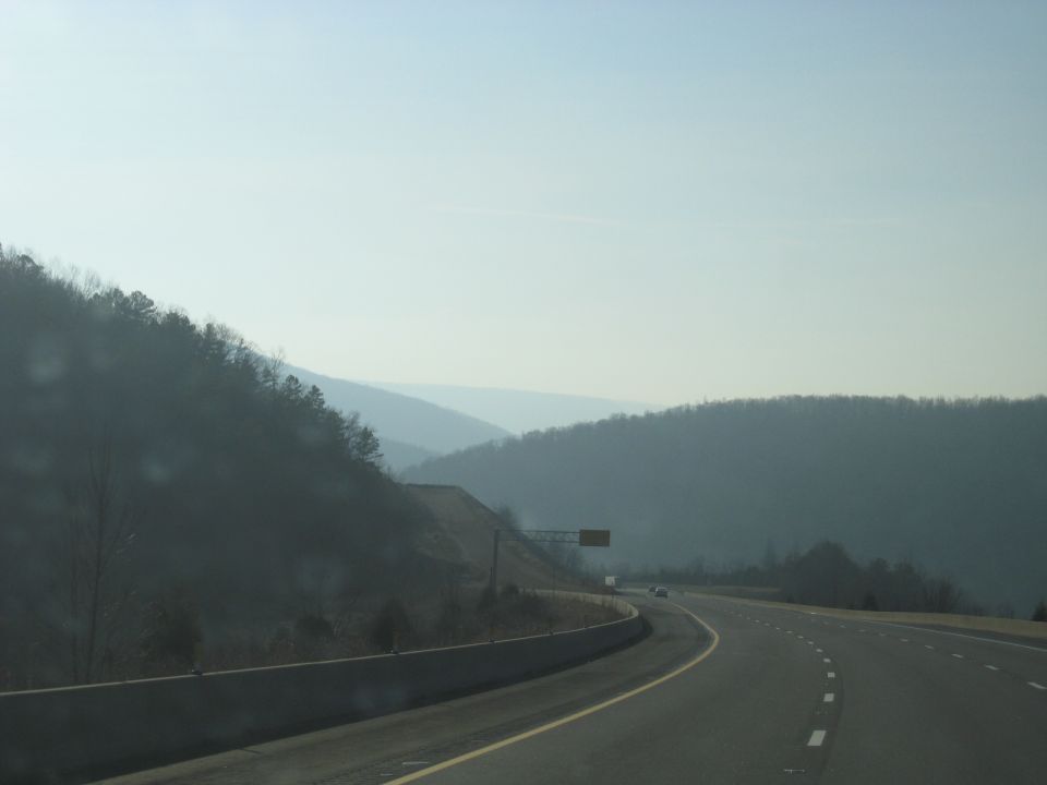 Curving highway with concrete barrier and forested ridges in the distance