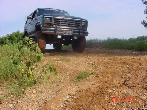 1986 Ford Bronco - 1986 Ford Bronco navigates a dusty, off-road path under a clear sky.