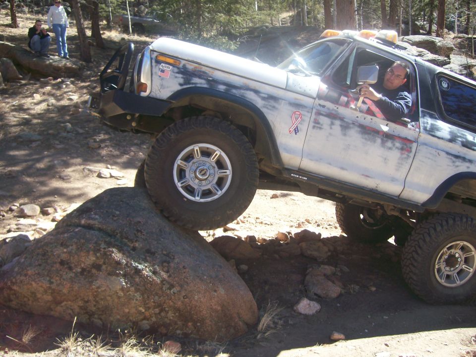 White and blue Ford Bronco off-roading over a large rock.