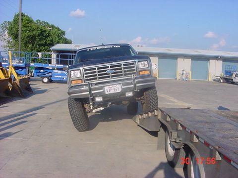 1986 Ford Bronco - A lifted Ford Bronco is being loaded onto a trailer, with a construction site in the background.