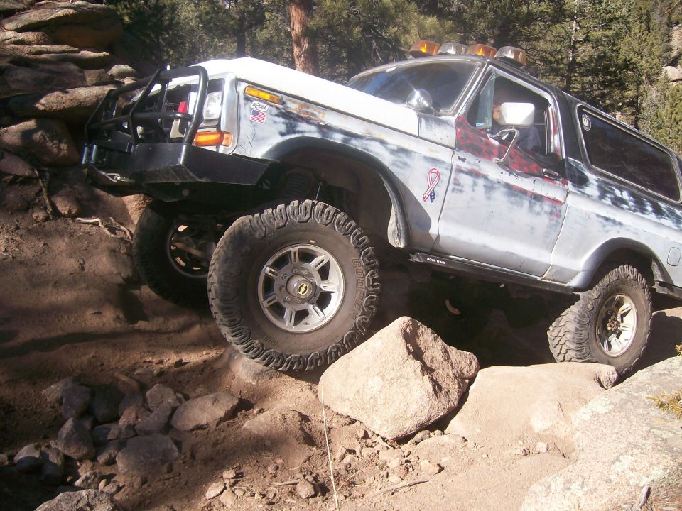 Off-road 1993 Ford Bronco climbing over rocks with large tires and custom bumper.