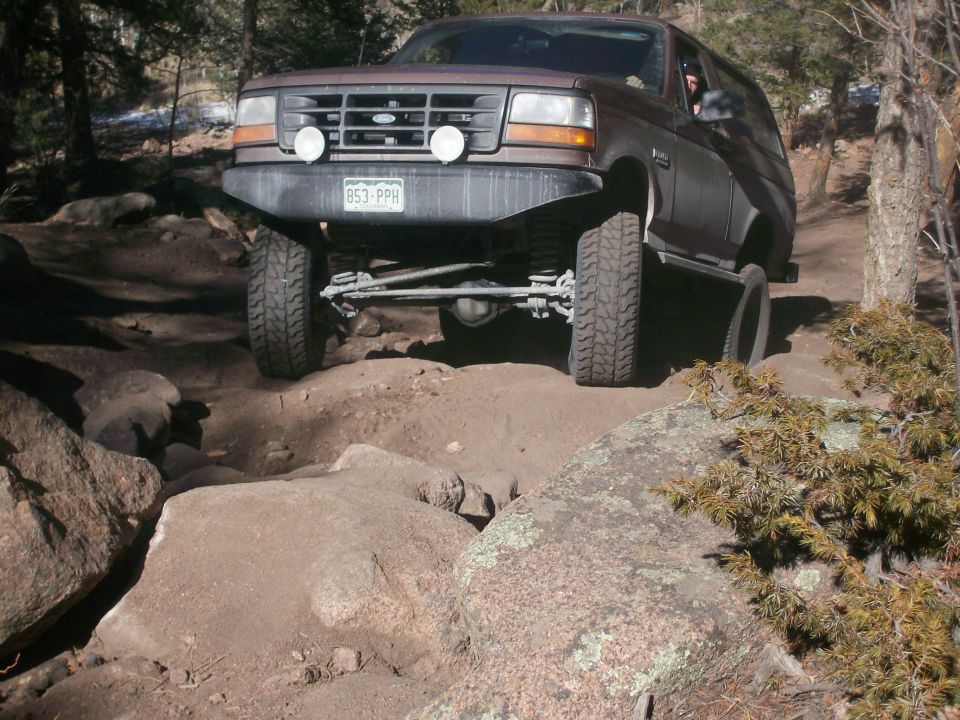 Brown 1993 Ford Bronco driving on a rocky off-road trail.