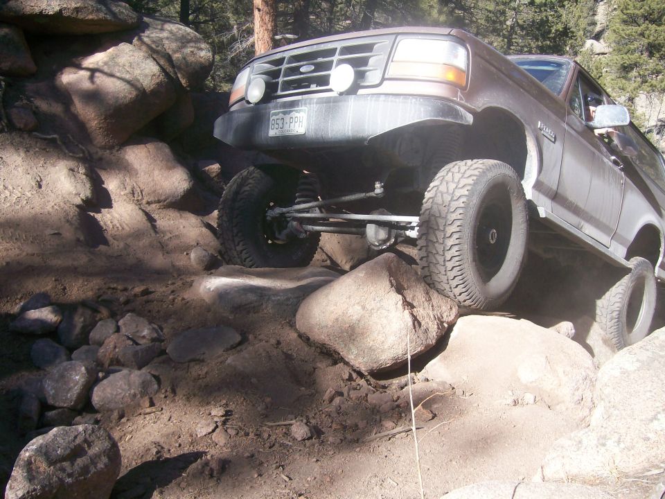 Brown Ford Bronco off-roading, front tire lifted over a boulder.
