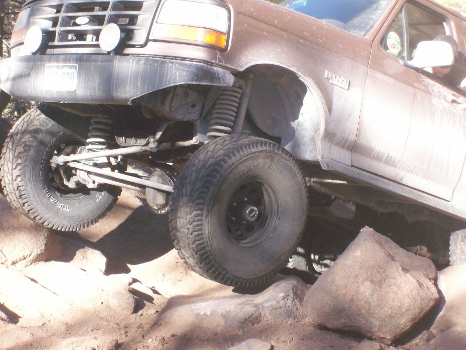 Brown Ford Bronco front driver's side navigating rocks, showing suspension and tires.