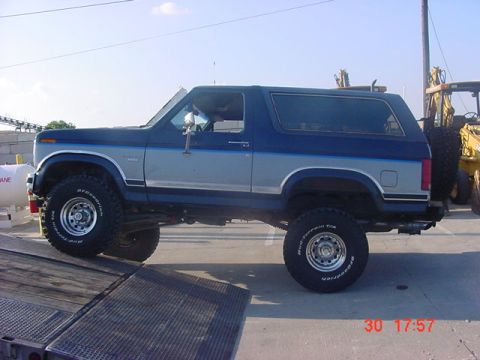 1986 Ford Bronco - Side view of a lifted 1986 Ford Bronco with off-road tires and a spare tire on the back.