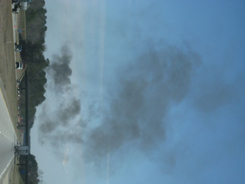 Sideways photo of heavy smoke over a highway shoulder with parked vehicles