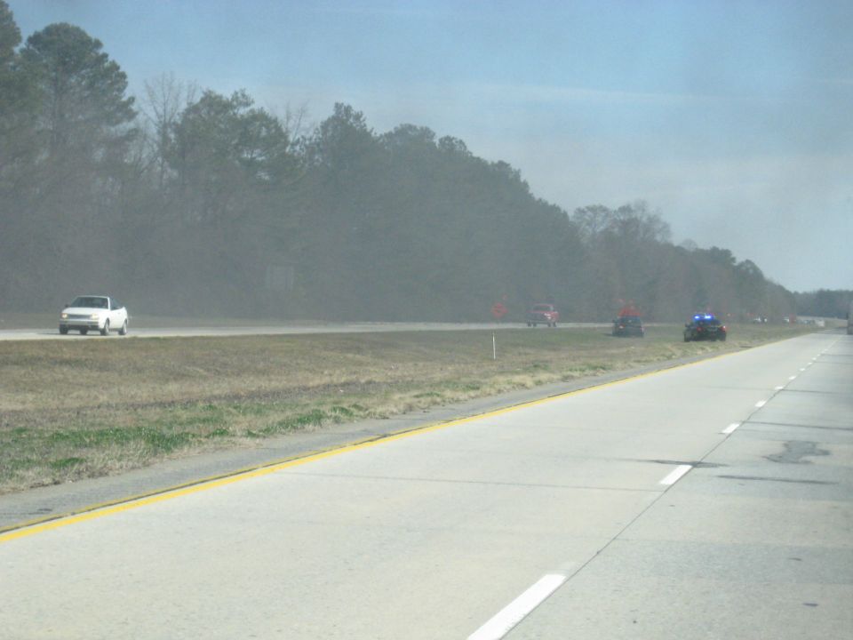 Highway with smoke haze, a white pickup, and emergency vehicles with lights