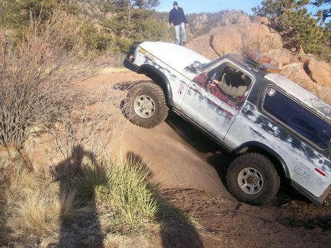1993 Ford Bronco - A white and black Ford Bronco is navigating a steep, rocky dirt trail with a person standing on a ridge in the background. The vehicle has…