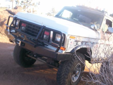 1993 Ford Bronco - A white Ford Bronco with a black brush guard and aftermarket bumper is parked on a dirt path with dry brush in the foreground.