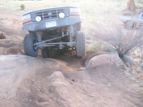 1993 Ford Bronco - A lifted 1993 Ford Bronco is shown at an extreme angle, navigating a rocky, off-road trail. The front tire is raised high as the vehicle cl…