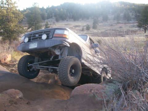 1993 Ford Bronco - A lifted 1993 Ford Bronco is navigating a rocky, off-road trail with its front passenger-side tire elevated.