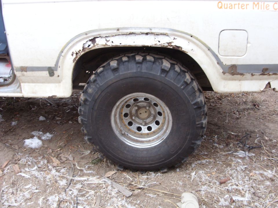 White Ford Bronco rear passenger side with off-road tire and rust.