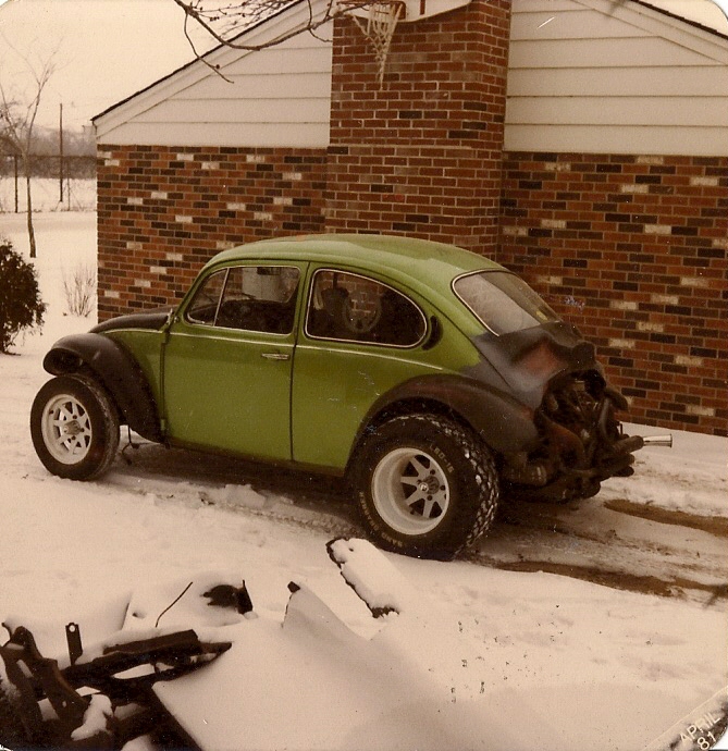 Lime green modified VW Beetle with off-road tires and exposed engine in the snow.
