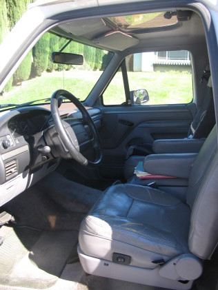 1988 Ford Bronco - The interior of a truck or SUV shows a gray leather driver's seat, steering wheel, and dashboard. The sun visor is open, revealing a sunroo…