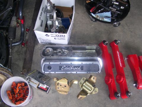 1990 Ford Mustang - Various automotive parts, including Edelbrock valve covers and red suspension components, are displayed on a garage floor.