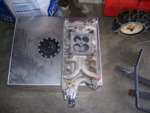 1990 Ford Mustang - An aluminum fuel tank and an Edelbrock intake manifold are displayed on a concrete floor.