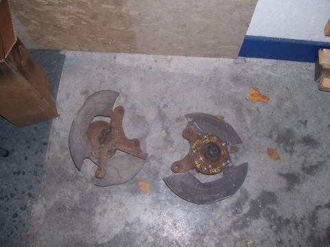 1990 Ford Mustang - Two rusty brake rotor dust shields with hubs are lying on a concrete floor. One dust shield has yellow markings that read "MUSTANG RH" and…