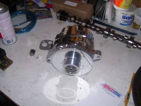 1990 Ford Mustang - A chrome alternator sits on a workbench next to a camshaft, a can of spray lubricant, and a roll of blue wire. A notepad with the AMSOIL lo…