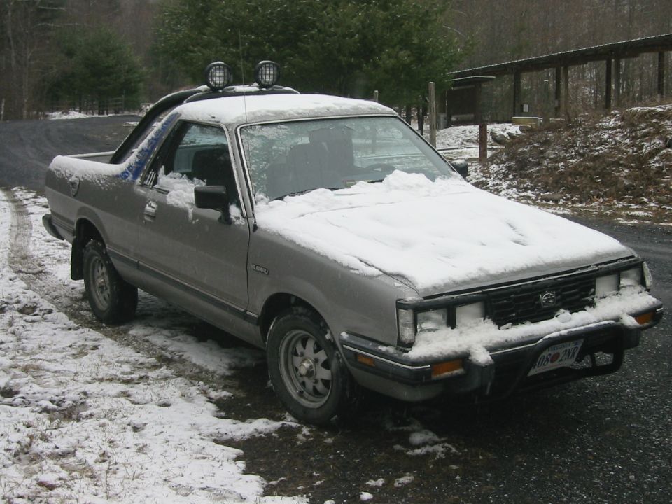 Silver Subaru Brat with snow on it, parked outdoors.