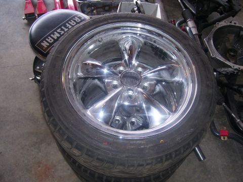 1990 Ford Mustang - A close-up view of a chrome five-spoke wheel and tire, likely for a classic car. The wheel is shiny and reflective, with a black tire featu…