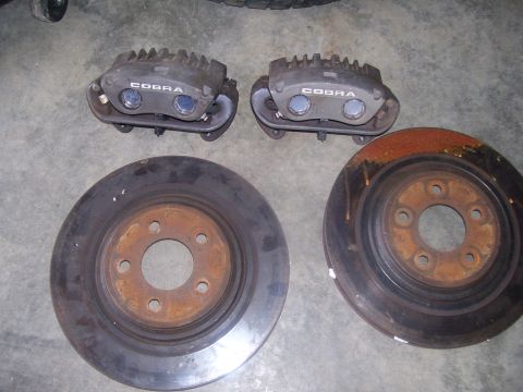 1990 Ford Mustang - Two Cobra brake calipers and two brake rotors are laid out on a concrete surface. The brake rotors show significant rust.