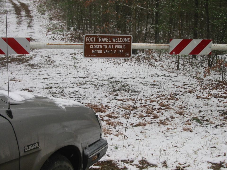 Grey Subaru parked in front of a closed gate on a snowy road.