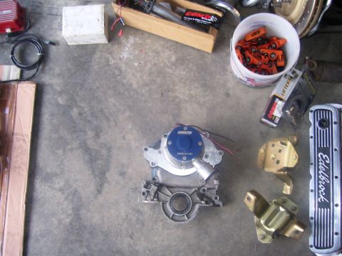 1990 Ford Mustang - Various engine parts are laid out on a concrete surface, including a water pump, valve covers, and a bucket filled with lifters.