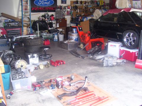 1990 Ford Mustang - A black 1990 Ford Mustang is parked in a cluttered garage next to a snowblower and various car parts. The car has chrome wheels and a red c…
