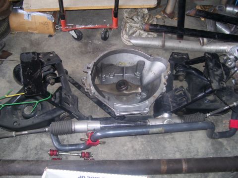 1990 Ford Mustang - A collection of car parts, including a transmission bell housing, suspension components, and a steering rack, are laid out on a concrete fl…