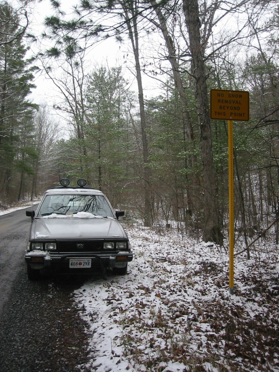 Silver Subaru station wagon parked on a snowy gravel road next to a "No Snow Removal" sign.