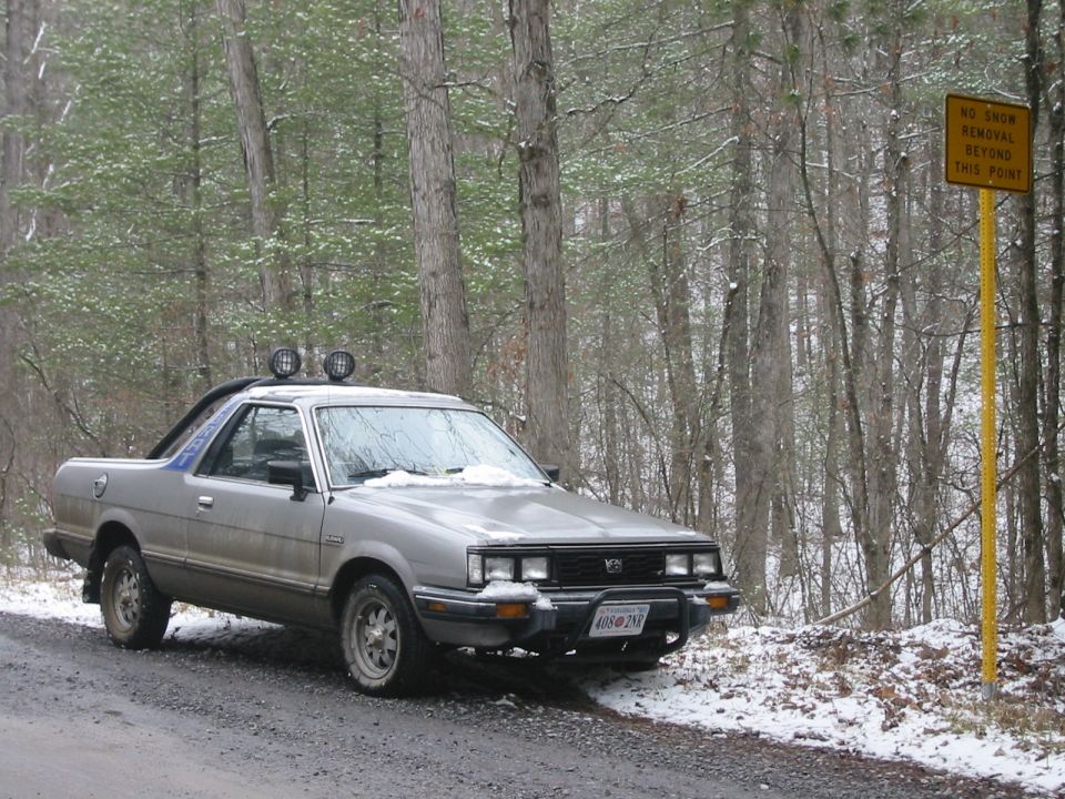 Silver Subaru Brat parked on a snowy forest road next to a "No Snow Removal Beyond This Point" sign.