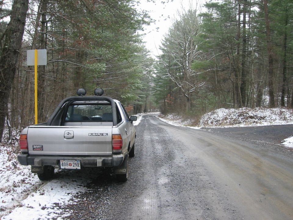 Silver 1986 Subaru Brat parked on a snowy gravel road.