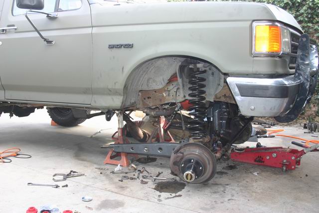 1991 Ford Bronco front suspension disassembled, supported by jack stands and a red jack.