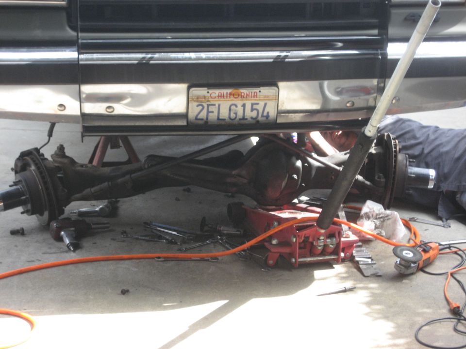 Underbody of a vehicle being worked on, with tools and a mechanic visible.
