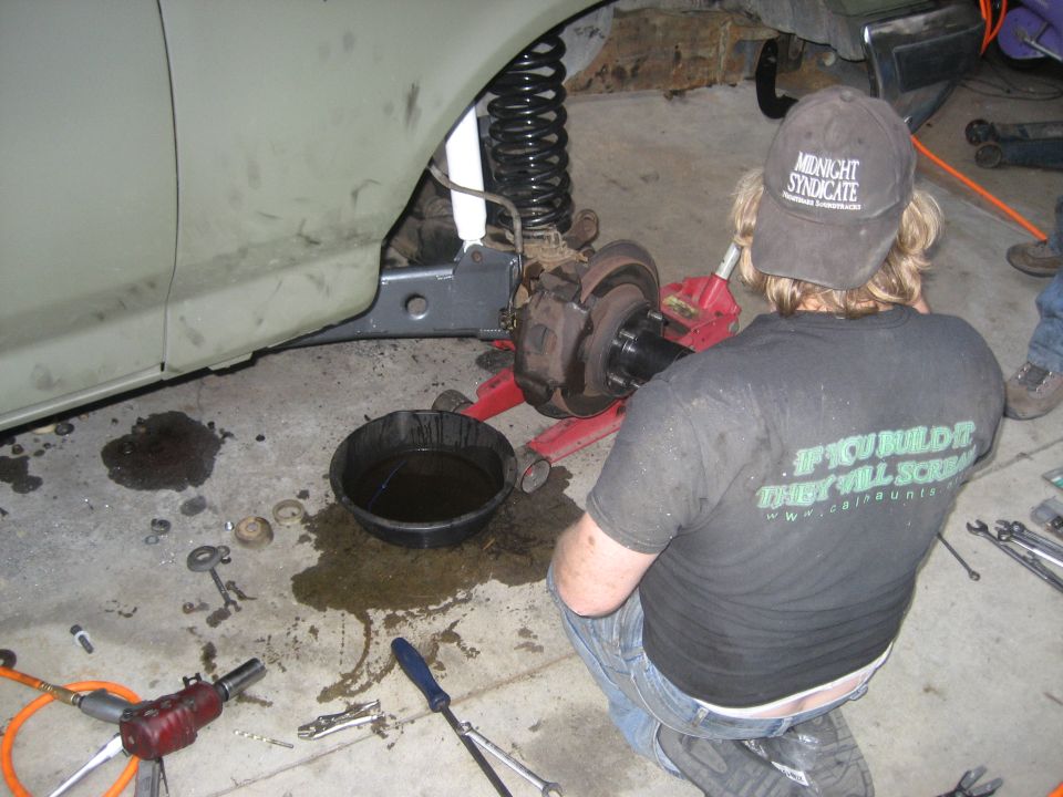 Person working on front brake and suspension of a light green vehicle, wheel removed.