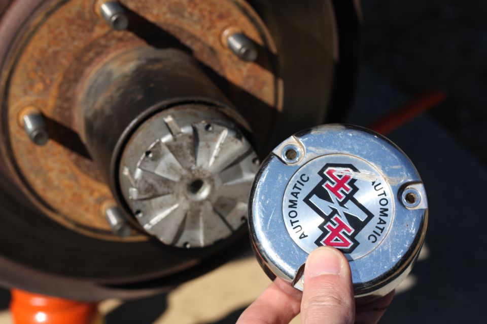 Chrome 4x4 Automatic hubcap held in front of a rusty wheel hub and brake rotor.