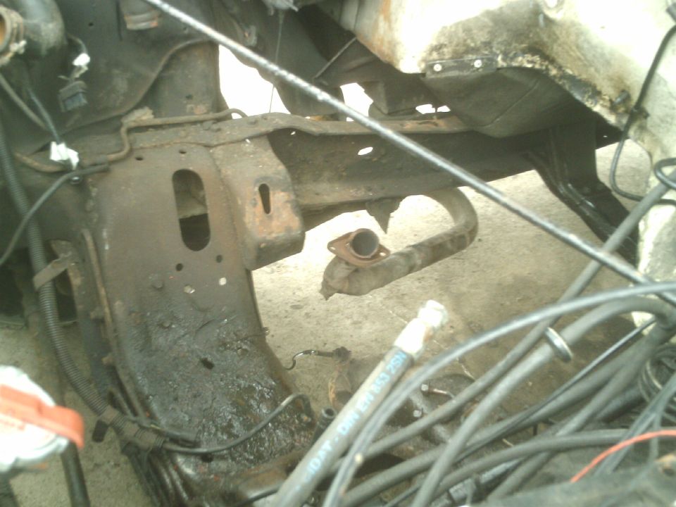Rusted engine bay and frame of a vehicle with hoses and wiring.