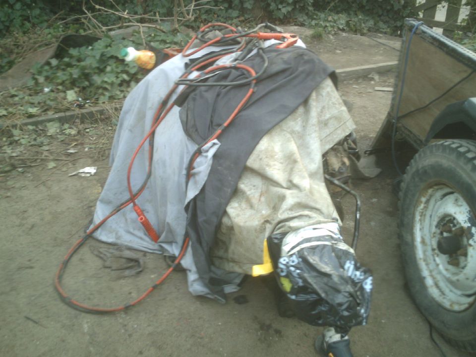 Vehicle covered by tarps and cables, with a tire visible.