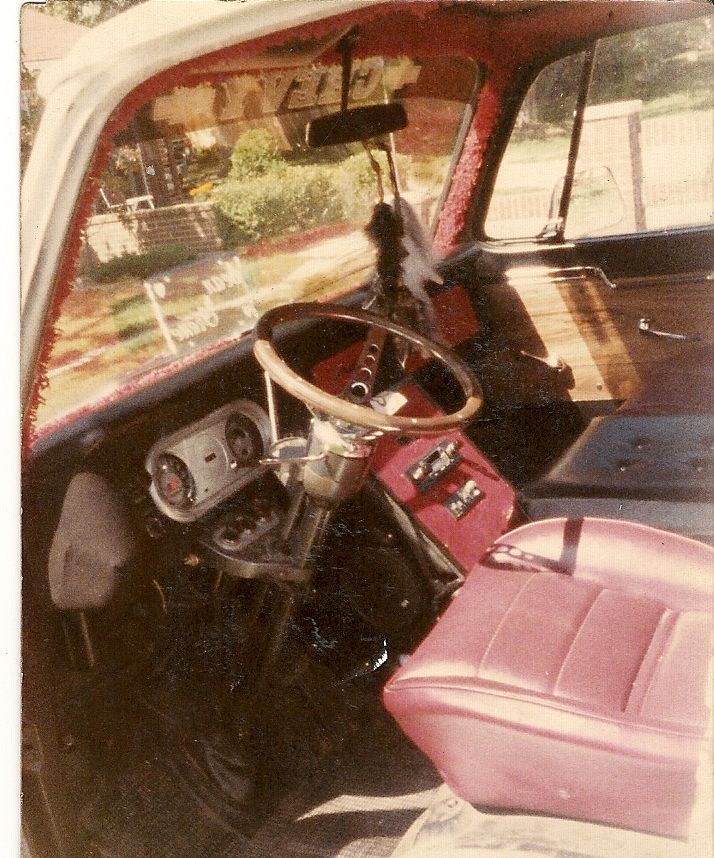 Interior view of a classic vehicle with a wood steering wheel, red dashboard, and pink seat.